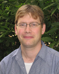 Gordon Berman standing outside before a large tropical bush